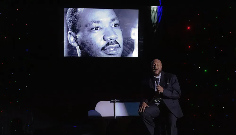 A person is performing on stage with an image of Martin Luther King Jr projected behind them