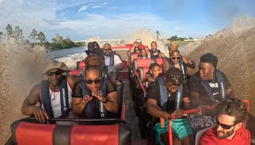 A group of people wearing life vests are enjoying a thrilling boat ride as water splashes around them.
