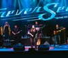 A band performs on stage under a large lit sign that says Forever Seger - The Silver Bullet Experience with a date of Saturday August 3 indicated below