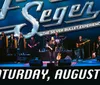 A band performs on stage under a large lit sign that says Forever Seger - The Silver Bullet Experience with a date of Saturday August 3 indicated below