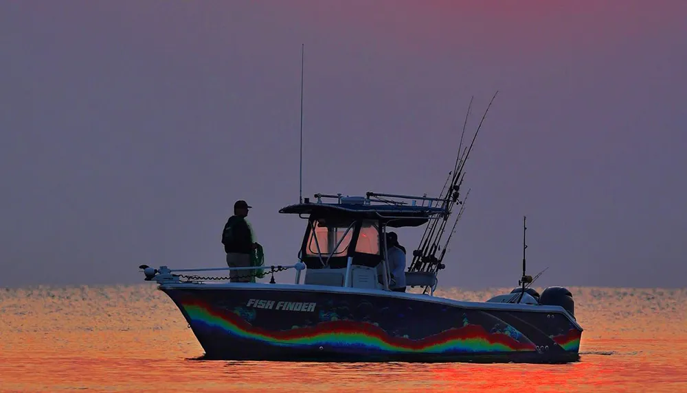 A person is standing on a fishing boat adorned with a colorful design on its hull set against a serene orange-hued seascape at sunset or sunrise