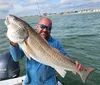 A man is smiling and holding up a large fish he caught while on a boat in the sea