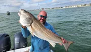 A man is smiling and holding up a large fish he caught while on a boat in the sea.