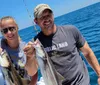 A man and a woman are smiling and posing with two freshly caught fish on a boat with the ocean in the background