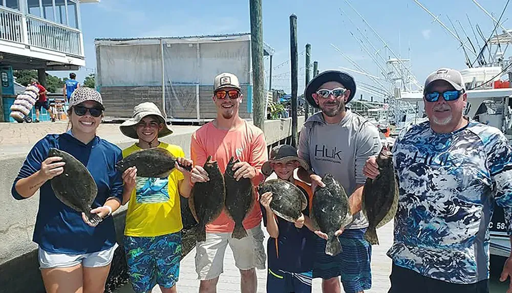 A group of people are posing with their catch of fish at a marina on a sunny day