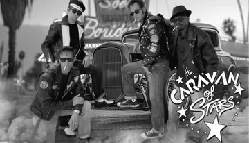 Four men in leather jackets and sunglasses pose in front of a vintage car with 