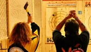 Two people are engaged in axe throwing, aiming at wooden targets with marked scoring zones.