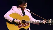 A person in a pink jacket is playing an acoustic guitar on stage.