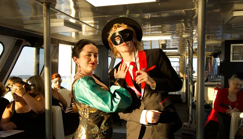 Two people in costume one with a mask pose together on a boat while others sit in the background
