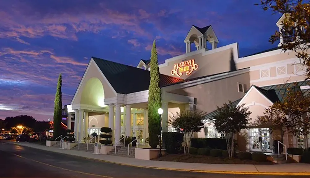 The image shows a well-lit theater entrance at dusk with a prominent sign that reads Alabama Theatre under a colorful evening sky