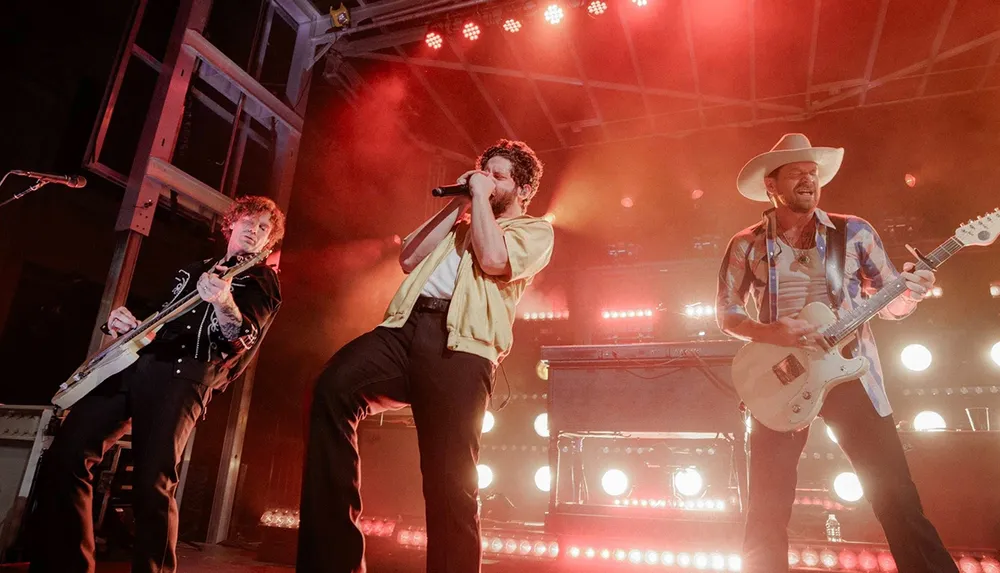 Three musicians are performing energetically on stage under bright lights