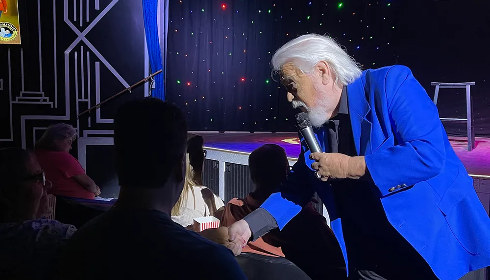 An entertainer in a blue suit interacts with the audience during a stage performance