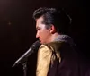 A person in a red jacket holds a microphone with the text Elvis Tribute Maxlee James displayed prominently