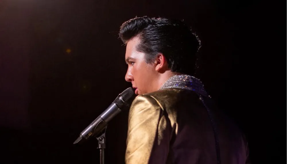 A man dressed in a sparkling gold jacket is singing into a microphone on stage