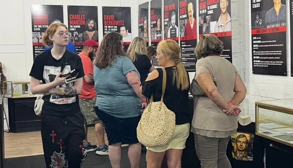People are observing posters about infamous criminals in a display or exhibition setting