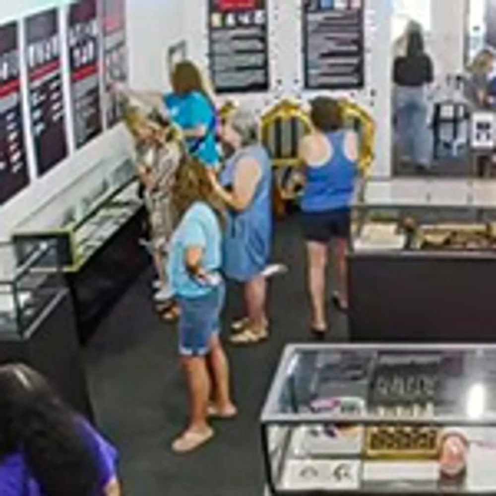 The image shows a group of people observing displays in a museum or exhibit setting
