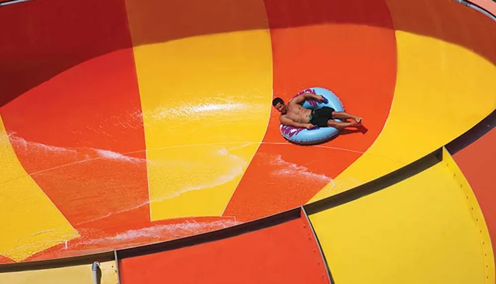 A person is enjoying a ride on a colorful enclosed water slide in an inflatable ring