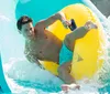 A person is joyfully sliding down a water slide on a yellow inflatable ring