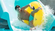 A person is joyfully sliding down a water slide on a yellow inflatable ring.