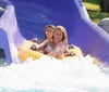 A person is joyfully sliding down a water slide on a yellow inflatable ring