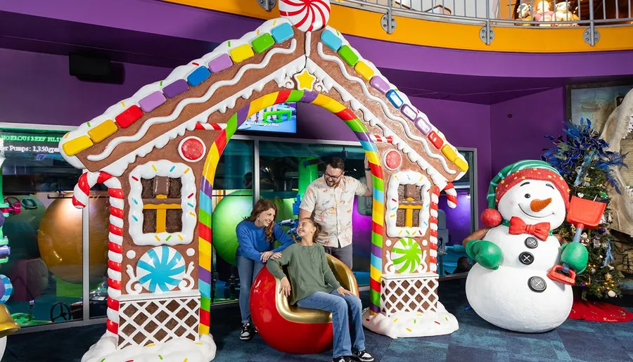 A family is enjoying a festive setting with a brightly decorated gingerbread house and a cheerful snowman.