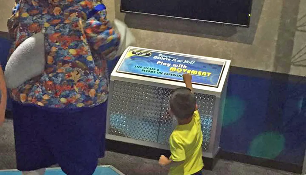 A child in a yellow shirt is interacting with an exhibit at a Ripleys Believe It or Not attraction while another person watches on