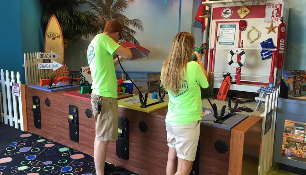 Two people are playing a shooting arcade game in a colorful room with a beach theme