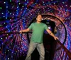 A person stands on a bridge inside a dazzling tunnel-like space with walls covered in colorful luminous patterns