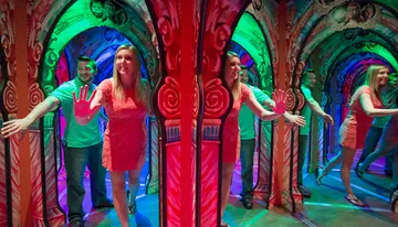 A woman and a man are navigating through a colorful mirror maze, creating multiple reflections.