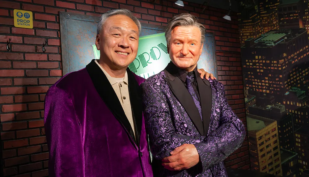 Two men in vibrant suits pose together in front of a comedy club backdrop