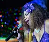 A group of performers in formal attire is on stage singing and entertaining an audience under colorful stage lighting and a backdrop that reads Motor City Musical