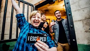 A group of people celebrate escaping from an escape room, with one person holding a sign that says 
