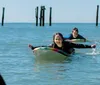 Two people are wearing wetsuits and lying on surfboards paddling in the ocean