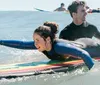 Two people are wearing wetsuits and lying on surfboards paddling in the ocean