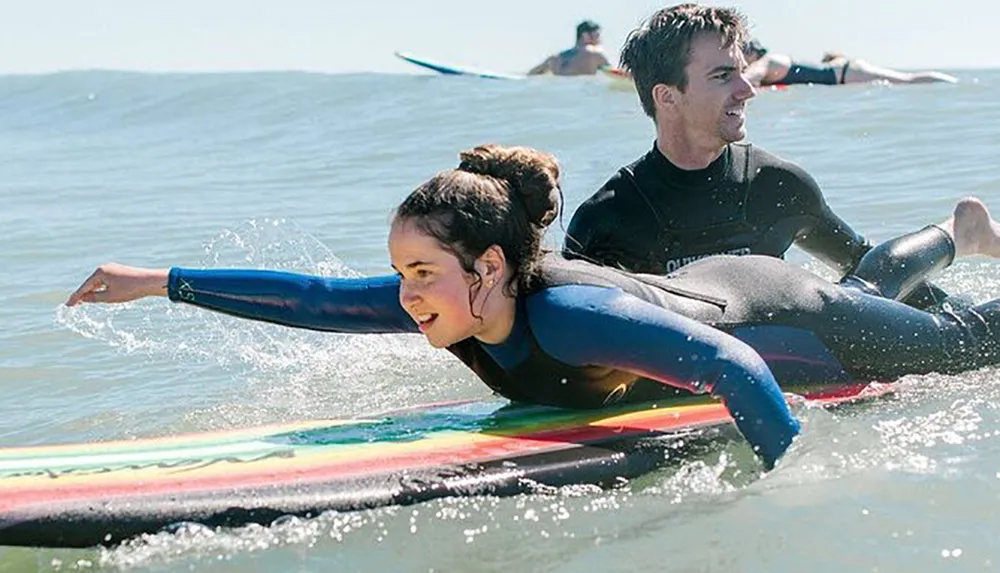 Two people are wearing wetsuits and lying on surfboards paddling in the ocean