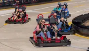 People are enjoying a ride in go-karts on a sunny day at a track.