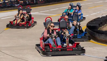 People are enjoying a ride in go-karts on a sunny day at a track.