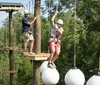 Two people are navigating an outdoor high ropes course among the trees equipped with safety harnesses and helmets