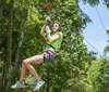 A person wearing a red helmet and a harness is enthusiastically zip-lining amidst green foliage