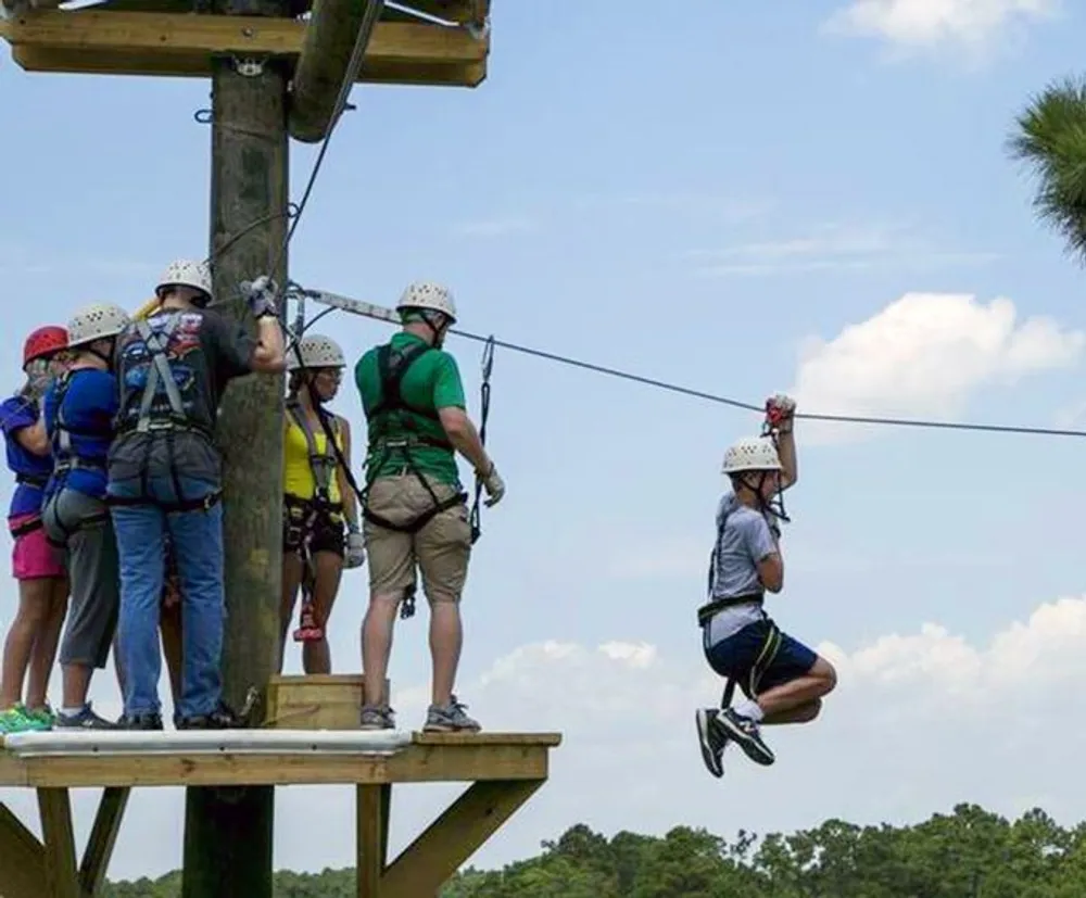 People equipped with safety harnesses and helmets are participating in a zip-lining adventure with one person actively gliding down the line