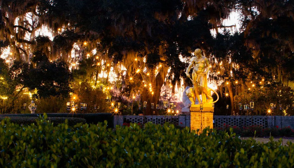 The image shows a gilded statue bathed in warm light set against a backdrop of lush trees draped with Spanish moss and illuminated by twinkling lights as evening falls