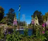The image shows a tranquil pond with vibrant water lilies in the foreground and an imposing white sculpture of figures in the background all set amidst lush greenery