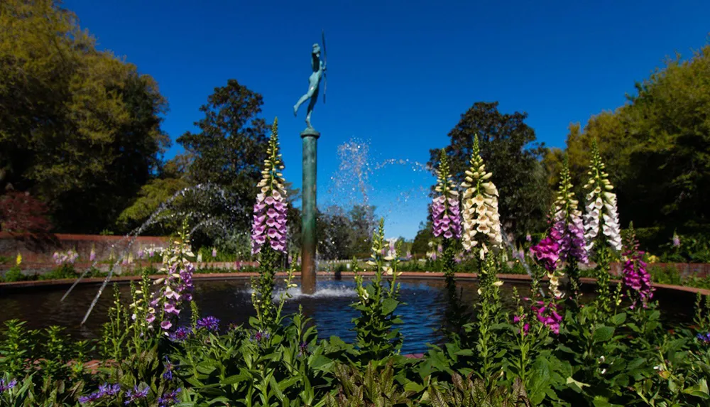 A serene garden scene with a statue atop a fountain surrounded by vibrant flowering plants and cascading water