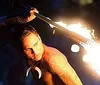 A group of performers engages in a traditional fire dance with a central figure manipulating flames while others dance around him against a dramatically lit backdrop