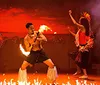 A group of performers engages in a traditional fire dance with a central figure manipulating flames while others dance around him against a dramatically lit backdrop