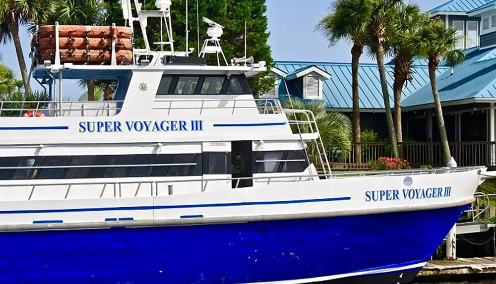 The image shows a blue and white boat named Super Voyager III docked near palm trees in front of a building with a blue roof