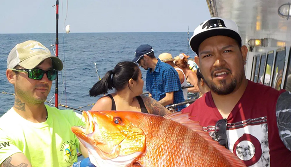 A man is holding a large colorful fish aboard a boat with other people around possibly after a successful fishing trip