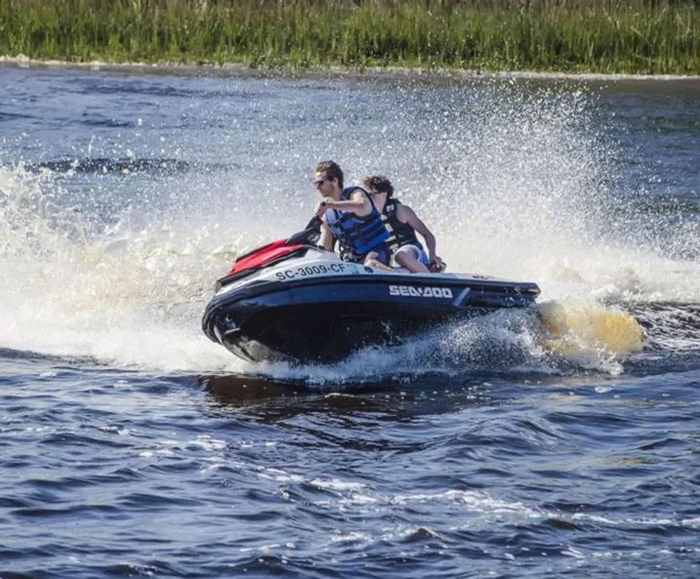 Two people are riding a jet ski with water splashing around them as they speed across a lake
