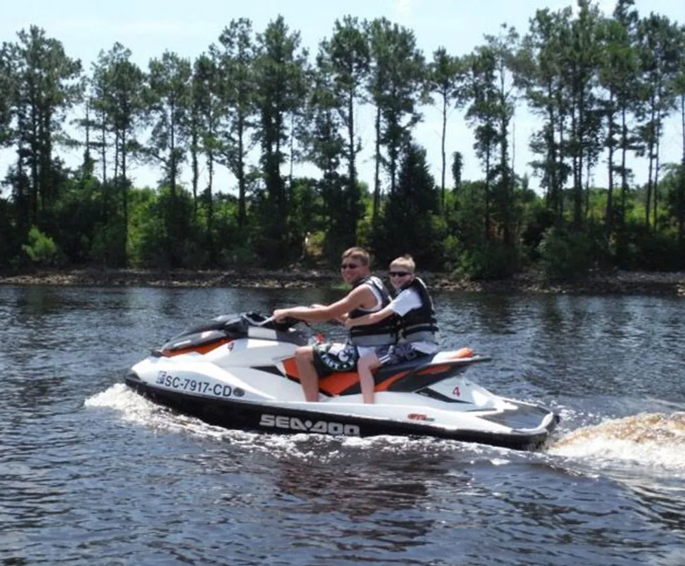 Two people are riding a jet ski on a body of water with trees in the background