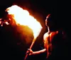 A performer with traditional tattoos is demonstrating a fire dance at night skillfully manipulating flaming objects